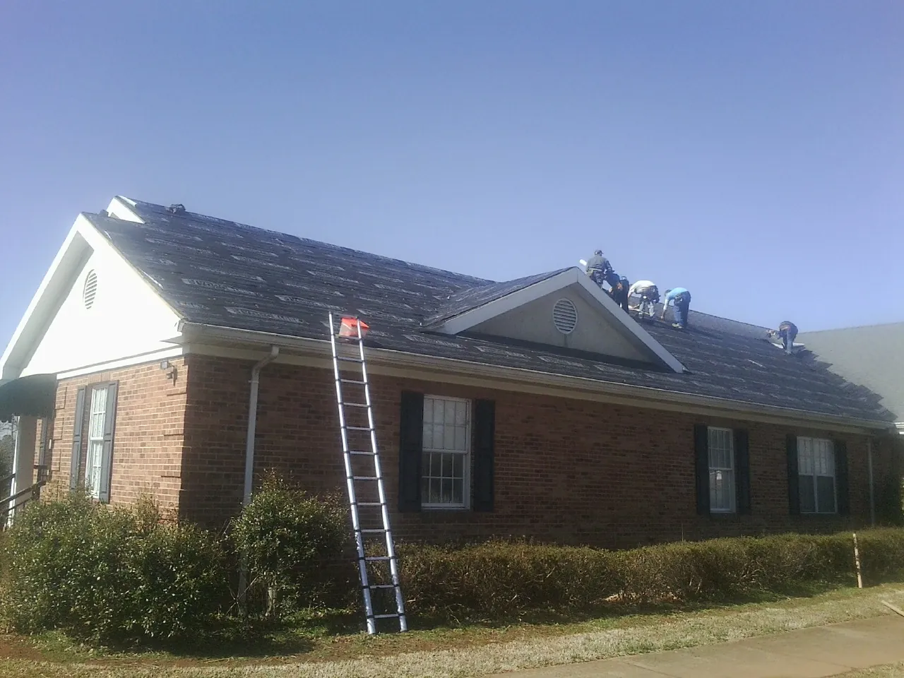 Crew tearing shingles off a brick ranch roof with a ladder set — Emergency Roof Repair work by our crew in Yorktown